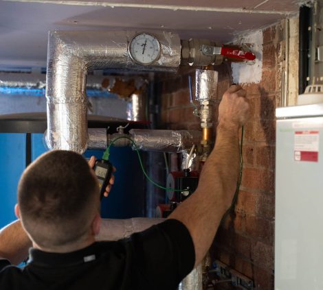 Water hygiene engineer inspecting commercial hot water pipework and pressure gauge