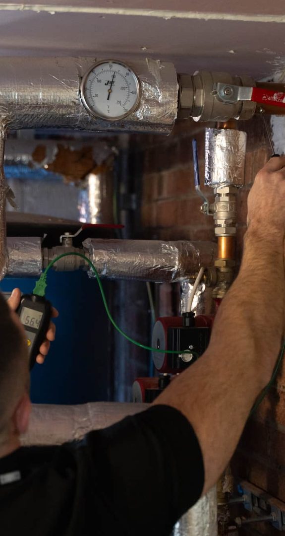 Water hygiene engineer inspecting commercial hot water pipework and pressure gauge