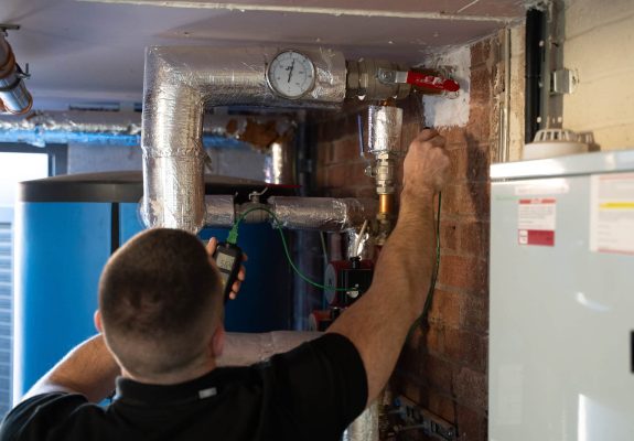 Water hygiene engineer inspecting commercial hot water pipework and pressure gauge